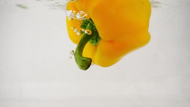 One fresh yellow bell paprika pepper falls into water on center with splashes and bubbles - Video