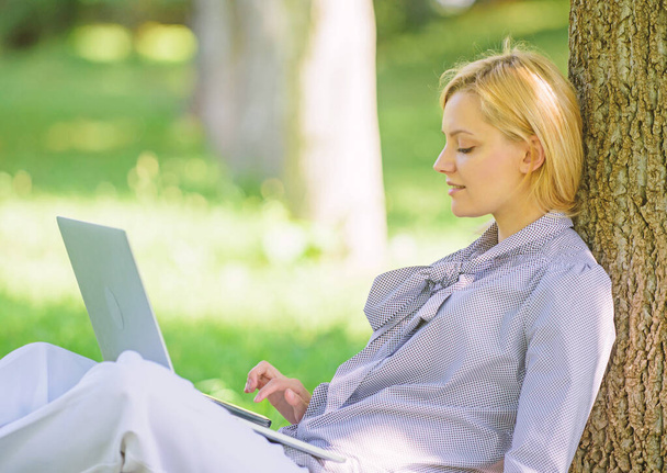 Girl work with laptop in park sit on grass. Natural environment office. Work outdoors benefits. Education technology and internet concept. Woman with laptop computer work outdoors lean on tree trunk - Photo, image