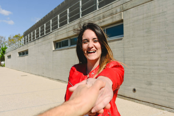 Kırmızı ceketli genç kadın nişanlısı tarafından gülümseyerek elini tutarak - Fotoğraf, Görsel