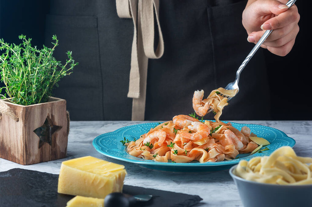 Cropped photo, a girl wrapped a spaghetti on a fork. Mafaldin pasta with tomato sauce, shrimp and thyme - Photo, Image