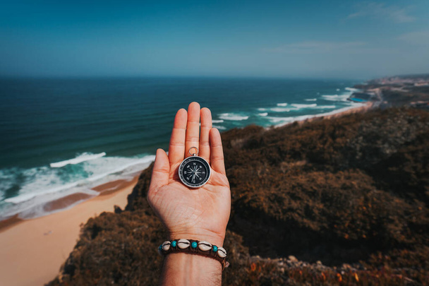 POV man hand with compass. Symbolling adventure-seeking concept against sea and waves in coastline in background - Foto, Imagen
