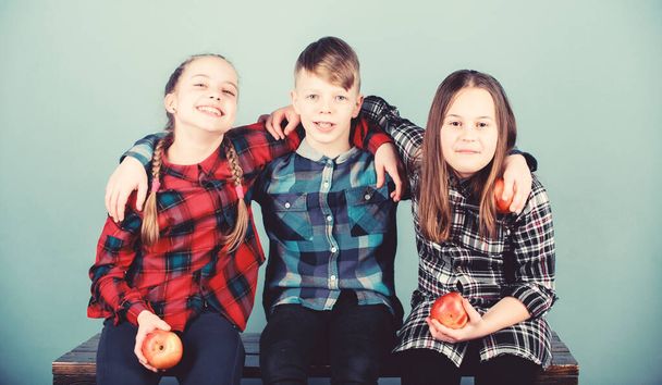 Boy and girls friends in similar checkered clothes eat apple. Teens with healthy snack. Healthy dieting and vitamin nutrition. Eat fruit and be healthy. Friends kids hug each other. Healthy lifestyle - Photo, Image