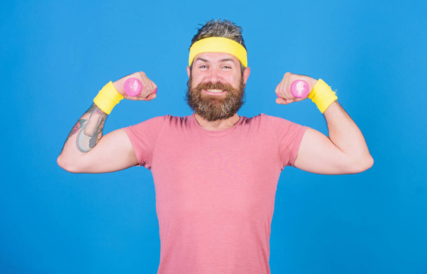 Athlete training with little dumbbell. Man bearded athlete exercising dumbbell. Motivated athlete guy. Athlete on way to stronger body. Healthy habits. Sportsman retro outfit training blue background - Fotó, kép