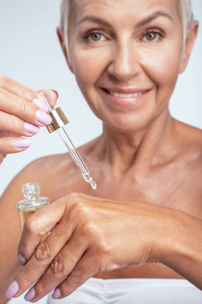 Beautiful senior woman smiling while putting serum on the back of her hand - Foto, Bild