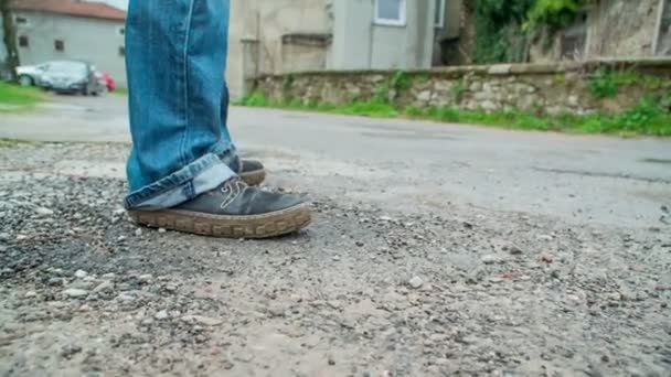 A man in jeans is standing on the road and is looking around. There are many old house around him. - Footage, Video