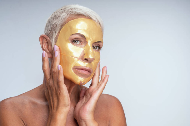 Attentive senior female putting gel mask on her face - 写真・画像
