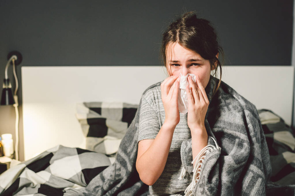 chora kobieta z katarem, siedząca w łóżku. Kobieta źle się czuje i kicha w sypialni. Kobieta trzymająca chusteczkę, objawy grypy. Koncepcja medyczna opieki zdrowotnej. Sezon zimna i grypy. kobieta z objawami alergii - Zdjęcie, obraz