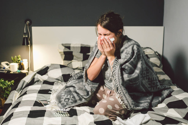 sick woman with runny nose, sitting in bed. woman feeling unwell and sneeze bedroom. Woman holding tissue ,flu symptoms. Healthcare medical concept. Cold And Flu Season. woman with allergy symptoms - Foto, Imagem