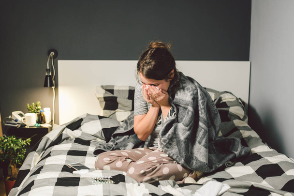 sick woman with runny nose, sitting in bed. woman feeling unwell and sneeze bedroom. Woman holding tissue ,flu symptoms. Healthcare medical concept. Cold And Flu Season. woman with allergy symptoms - Photo, image