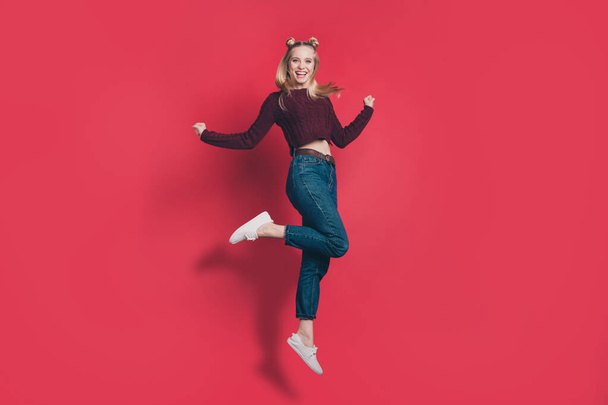 Full body profile photo of funny attractive lady jumping high rejoicing in flight wear knitted burgundy pullover and jeans isolated pastel red color background - Fotó, kép