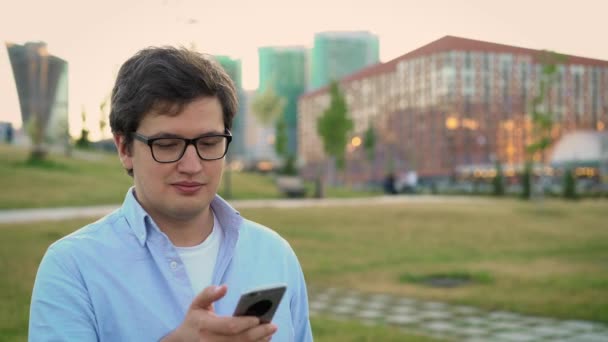 Portré felnőtt férfiról, aki mobiltelefont használ a park gyepén - Felvétel, videó