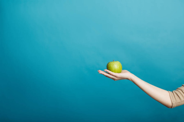 Image d'une main de fille tenant une pomme debout isolée sur un fond bleu
 - Photo, image