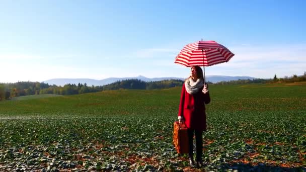 kobieta w płaszczu z walizką i parasolem na tle góry - Materiał filmowy, wideo