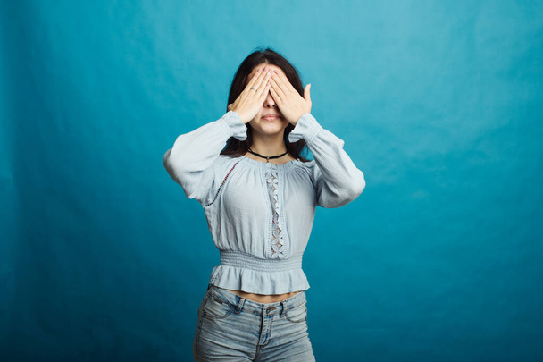Image of a happy young girl standing on a blue background covered her face with her hands - Photo, Image