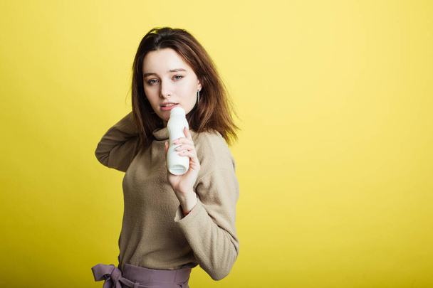 Image of a happy young girl standing isolated on a yellow background singing in a yogurt bottle - Fotó, kép