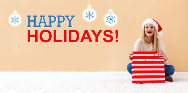 Happy holidays message with woman with Santa hat holding a shopping bag - Фото, зображення