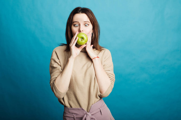 Image of a happy young girl standing on a blue background holding a green apple - Foto, Imagem