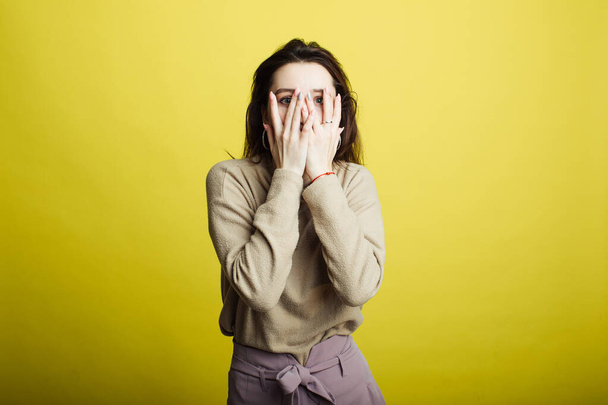 An image of a happy young girl standing isolated on a yellow background covered her face with her hands - 写真・画像