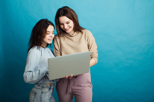 Image of happy young girls standing isolated over blue background and looking at laptop - Φωτογραφία, εικόνα