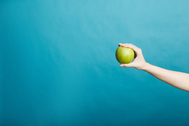 Bild einer Mädchenhand mit einem Apfel, der isoliert auf blauem Hintergrund steht - Foto, Bild