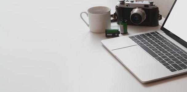 Schnappschuss von minimalem Arbeitsplatz mit Laptop und Kamera auf weißem Tisch und Kaffeetasse  - Foto, Bild