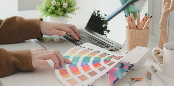 Gesneden foto van jonge professionele vrouwelijke ontwerper kiezen van de kleur voor haar project tijdens het typen op laptop computer  - Foto, afbeelding