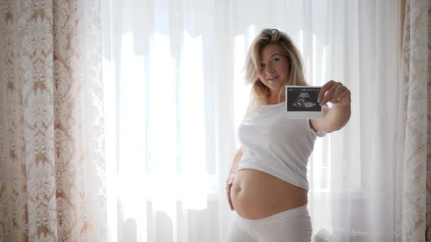 toekomstige moeder raakt haar naakt zwanger grote buik en toont een echo scan van het kind - Video