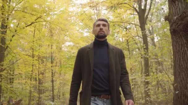 Close-up of a handsome confident Caucasian man in casual clothes walking in the forest . Guy with grey hair and brown eyes enjoying calm quiet autumn day alone. - Πλάνα, βίντεο