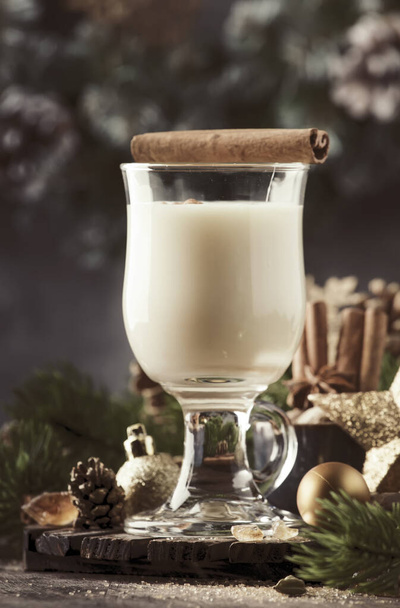 Christmas or New Year Eggnog alcoholic cocktail - hot winter drink with milk, eggs and rum, sprinkled with cinnamon and nutmeg in glass on gray background, copy space - Foto, imagen