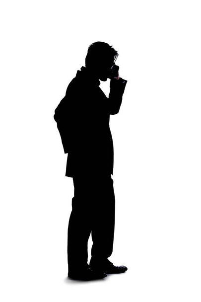 Full body silhouette of a businessman isolated on a white background. He is using a cell phone or mobile device to talk or send messages. - 写真・画像