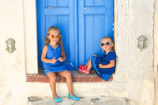 Маленькі милі сестри сидить біля старих синій дверей в грецькі села Emporio, Санторіні - Фото, зображення