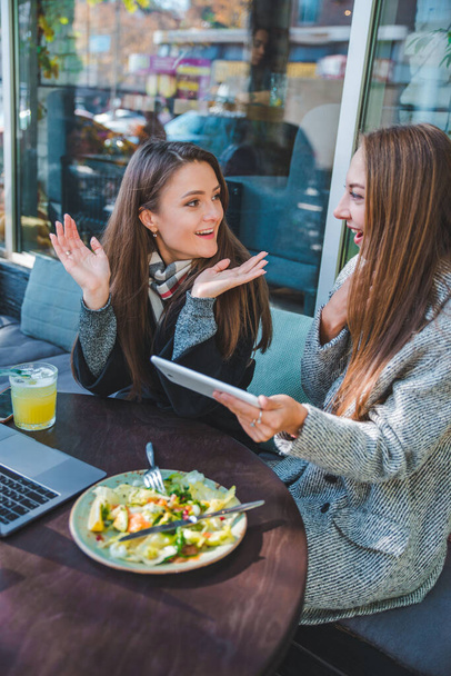 kaksi nuorta aikuista naista tapaavat ulkona kahvilassa työskentelemässä kannettavan tietokoneen kanssa
 - Valokuva, kuva