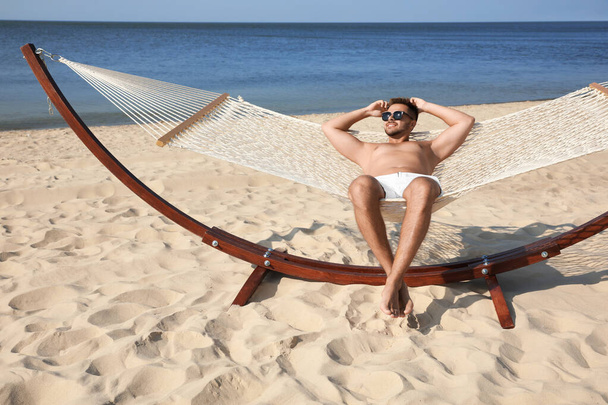 Young man relaxing in hammock on beach - Фото, изображение