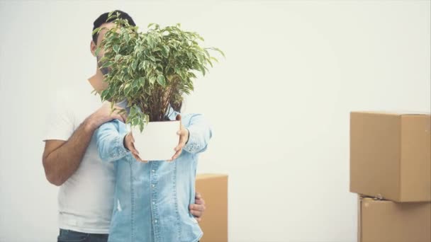 A fiatal pár együtt költözött egy új lakásba. Egy zöld virágcserepet tartanak és mosolyognak. Felvétel, animáció. 4k. - Felvétel, videó