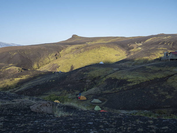 Πολύχρωμες σκηνές και καλύβα Botnar βουνό στην Ισλανδία για Laugavegur πεζοπορία μονοπάτι, πράσινη κοιλάδα σε ηφαιστειακό τοπίο μεταξύ των πεδίων λάβας. Νωρίς το πρωί ανατολή άποψη. - Φωτογραφία, εικόνα