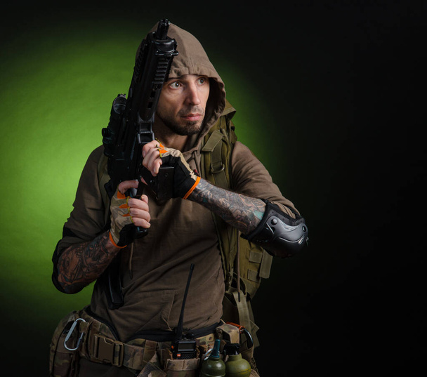 muž stalker s pistolí s optickým zaměřovačem a batohem na tmavém pozadí - Fotografie, Obrázek