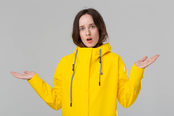 hübsches brünettes Mädchen in einem gelben Regenmantel, das Emotionen der Überraschung ausdrückt. Bereiten Sie sich auf schlechtes Wetter vor. - Foto, Bild