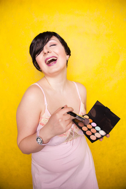 Happy plus size woman having fun with make-up palette set and brush. Professional multicolor eyeshadow face corrector palette. - Photo, Image