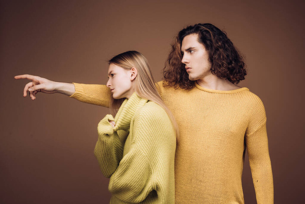 Portret of stylish confident male and female models with nature hairstyle wearing a yellow and green sweater and standing close together looking alluringly at camera. - Fotografie, Obrázek