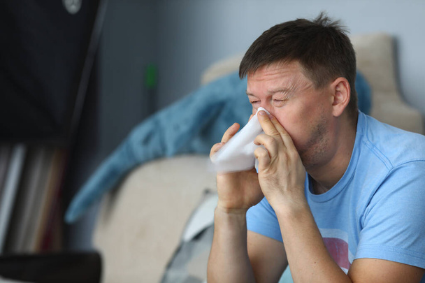 Ο άνθρωπος φυσάει τη μύτη του σε μια χαρτοπετσέτα ενώ κάθεται - Φωτογραφία, εικόνα