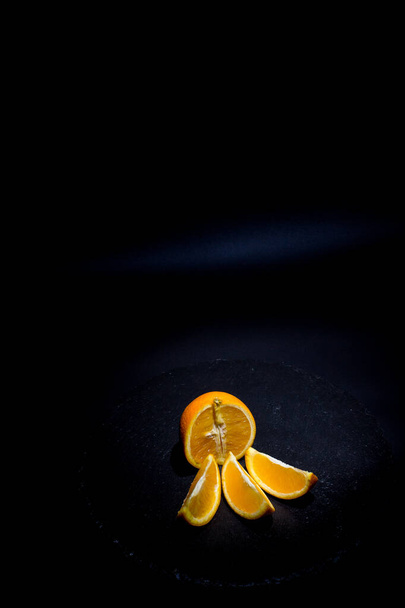Ripe orange and orange slices on a black background and black surface - Фото, изображение