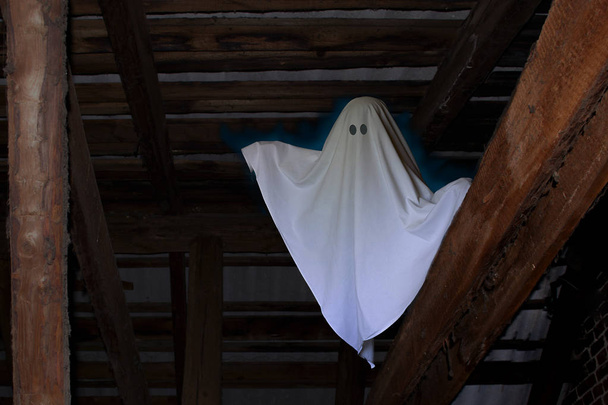  Fantasma sotto forma di foglio con due inquietanti occhi neri in una soffitta buia e polverosa
. - Foto, immagini