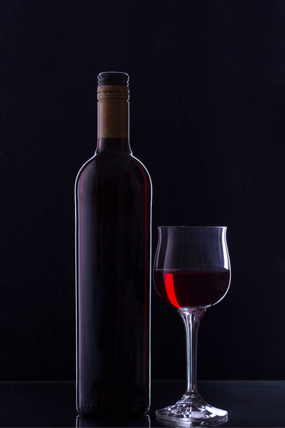 a bottle and a glass of red wine on a black background with backlight and side lighting. - Φωτογραφία, εικόνα