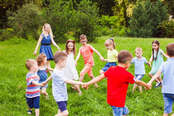 Счастливые дети танцуют в кругу на зеленой лужайке в парке
 - Фото, изображение