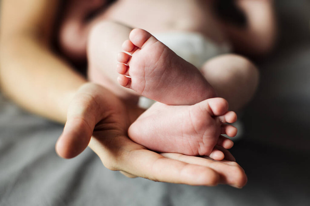 Anya újszülött baba lábat tart a kezében. Anya vigyáz a csecsemőre fürdés után. A szülők gyermekgondozása. Gyermekek egészségügyi ellátása és boldog család - Fotó, kép