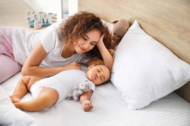 Young African-American woman and her sleeping baby on bed - 写真・画像