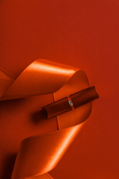 Lápiz labial de lujo y cinta de seda sobre fondo de vacaciones naranja, ma
 - Foto, Imagen