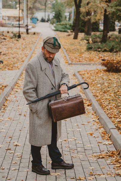 Man with carpetbag and coat is standing on autumn alley - Valokuva, kuva