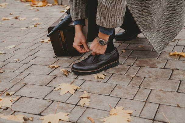 Gentleman is tying lace on brown shoe. Nearby is carpetbag - Fotoğraf, Görsel