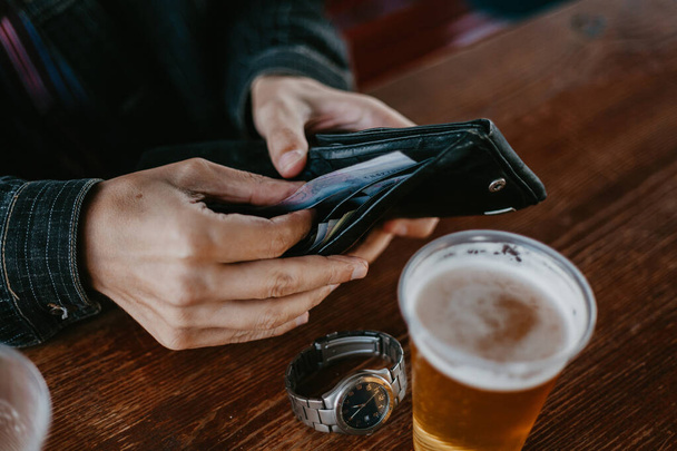 Hands get money from the wallet. Near glass of beer - Foto, Bild